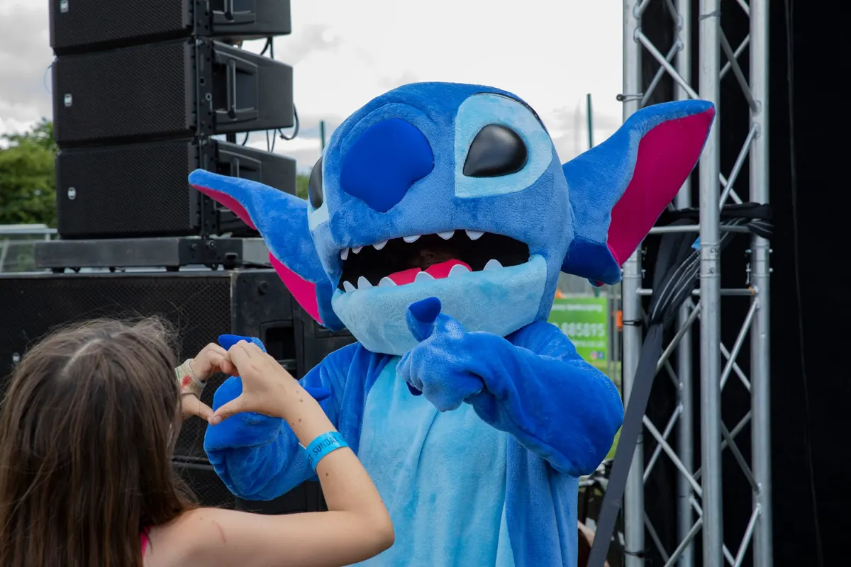 Stitch mascot posing with a young fan making a heart shape with her hands at Ely Fest.